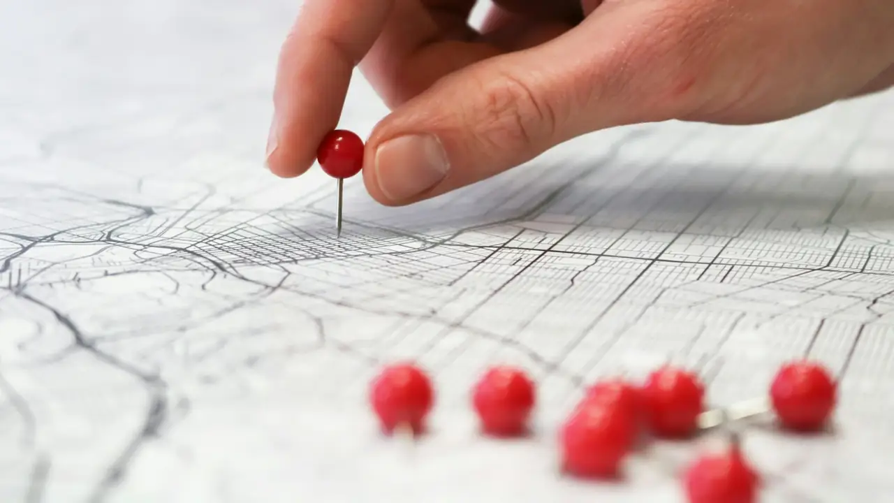 Main qui plante une épingle rouge sur un plan de ville